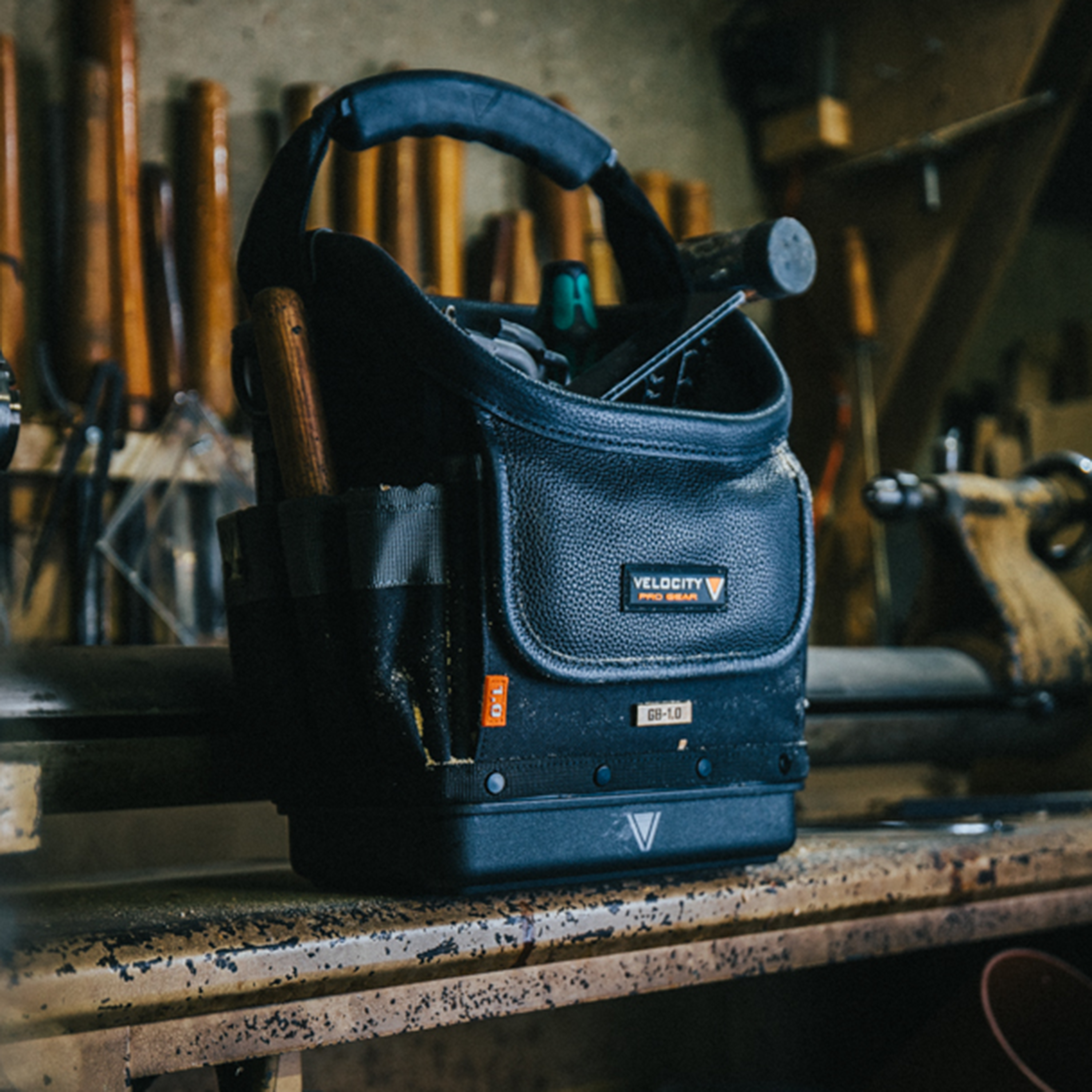 Velocity Rogue 1.0 Open Tote tool bag with tools in the top sitting on a workshop bench